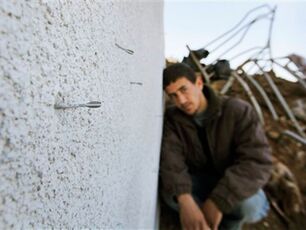 A Palestinian looks on as a small pointed metal dart known as a flechette, usually spread over a wide area in large numbers from a shell, is seen sticking out of the wall of a destroyed house in Mughraka, Gaza, on 21 January, 2009 (AP)