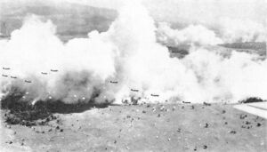 Небольшие силуэты на фоне облаков дыма, созданных для обеспечения маскировки, C-47 ВВС США сбрасывают батальон 503-го парашютного полка в Надзабе, Новая Гвинея. На переднем плане приземляется батальон, сброшенный несколькими минутами ранее. 5 сентября 1943 г.
