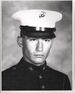 Head of a young white man wearing a white peaked cap with black visor and a dark military jacket.