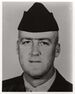 Head of a white man wearing a garrison cap and a dark military jacket over a light-colored shirt.