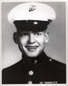 Head of a young white man with a big smile, wearing a white peaked cap with black visor and a dark military jacket.