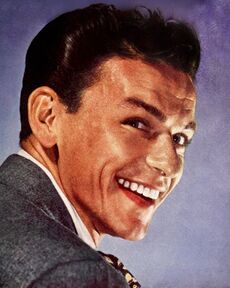 Close-up studio photograph of a young, smiling Sinatra with styled hair wearing a suit and tie