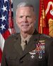 A color image of James Amos, a white male in his Marine Corps Service A uniform. He is not wearing a hat, several ribbons are visible as well as a rifle and pistol marksmanship badges and naval aviator insignia. The Marine Corps flag and United States flag are visible in the background.