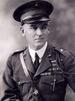 A black and white image of Logan Feland, a white male in his Marine Corps Service A uniform. He is wearing a hat several ribbons and a Fourragère. He also has a leather strap from his right shoulder to his left waist.