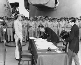 Министр иностранных дел Японии Мамору Сигэмицу подписывает акт о капитуляции Японии на борту американского военного корабля USS Missouri под наблюдением генерала Ричарда К. Сазерленда[en], 2 сентября 1945 года.