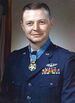 Head and shoulders of a man with short hair and a round face in a dark blue military jacket. Rows of ribbon bars and a winged pin are on his left breast and a medal hangs from a light blue ribbon around his neck.