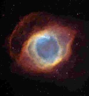 Цветное изображение планетарной туманности напоминает по форме глаз. В центре видна маленькая звезда, вокруг неё наблюдается голубоватое сияние, затем видны оранжевые полосы, после которых наблюдается красная оболочка.