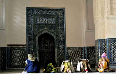 Несколько женщин молятся внутри здания. На стене есть ниша, в сторону которой молятся.