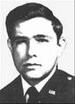 Head of a young white man with thick hair wearing a dark military jacket with a "U.S." pin on the lapel.